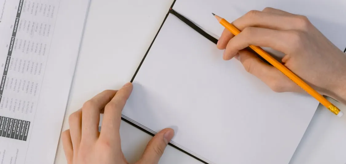 A blank notebook with a person holding a yellow pencil. With a planner in front of them